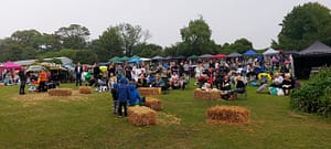 People outside at a festival type event. Mingling around haybales and tents for Martha’s Music on the Farm at Solley’s Ice Cream Parlour in Deal